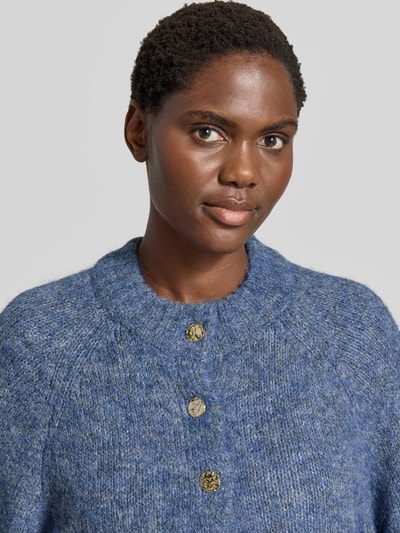 Frauenmodel trägt Relaxed Fit Cardigan mit Woll-Anteil Modell 'Benutta' von Neo Noir in Strick-Optik, Knopfleiste, meliertes Blau, Nahaufnahme Oberkörper. Elastischer Material-Mix, 1/2-Arm, Rückenlänge 54 cm, Ärmellänge 38 cm.