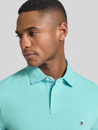 Männermodel trägt Regular Fit Poloshirt aus Baumwoll-Mix von Tommy Hilfiger, Optik: Unifarben, Logo-Stitching, Nahaufnahme Oberkörper.