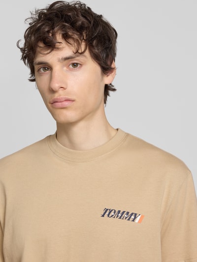 Männermodel trägt Regular Fit T-Shirt aus reiner Baumwolle von Tommy Jeans in Beige, unifarben mit Label Print, Nahaufnahme Oberkörper.