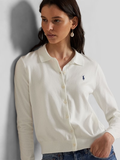 Modelka kobieca ma na sobie Slim Fit Strickjacke aus Baumwoll-Mix od Polo Ralph Lauren, jasny kolor, gładki wzór, drobny dzianinowy materiał, logo, długi rękaw, kołnierzyk koszulowy, zapięcie na guziki, mankiety i dół prążkowane, krój slim fit, bawełniany miks, zdjęcie całej sylwetki z przodu.