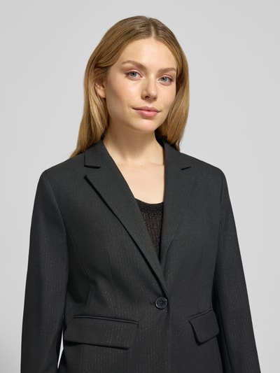 Modelka kobieca nosi Slim Fit Blazer mit Reverskragen od More & More, czarny, materiał z domieszką wiskozy, zapięcie na guzik, kieszenie z patkami, widok na górną część ciała z przodu.