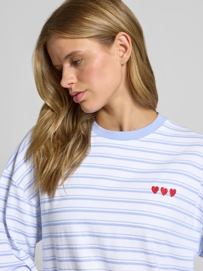 Frauenmodel trägt Relaxed Fit Sweatshirt mit Motiv-Stitching von REVIEW, weiße Baumwolle mit blauen Streifen, Nahaufnahme Oberkörper.