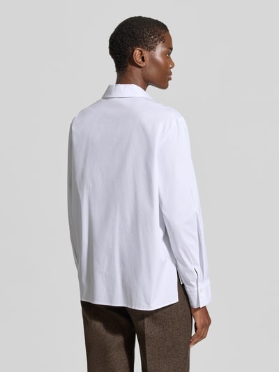 Frauenmodel trägt Bluse mit verlängertem Rücken Modell 'Berendine' von JOOP!, weiße Baumwoll-Mix mit Stretch-Anteil, Regular-Fit, Logo-Stitchings, Rückenlänge bei Größe 38: 66 cm, Ärmellänge: 65 cm, Hemdblusenkragen und Knopfleiste, Ganzkörperansicht Rückansicht.