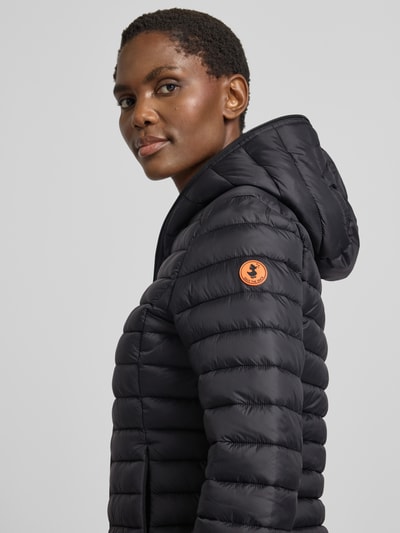 Frauenmodel trägt schwarze Steppjacke mit Zweiwege-Reißverschluss Modell 'DAISY' von Save The Duck, Kapuze, Nahaufnahme Oberkörper.