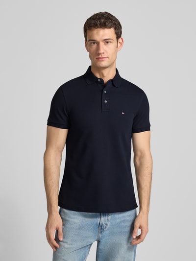 Männermodel trägt Slim Fit Poloshirt mit Stretch-Anteil van Tommy Hilfiger in donkerblauw, katoen-elastaan mix, voorkant, bovenlichaam.