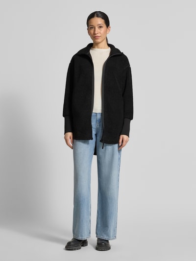 Frauenmodel trägt schwarze Fleecejacke mit Stehkragen Modell 'TOLA' von Didriksons, Relaxed-Fit, Reißverschluss, Ganzkörperansicht von vorne, Rückenlänge 83 cm, Schulterbreite 52 cm, Brustweite 47 cm, Ärmellänge 56 cm, Größe 36.