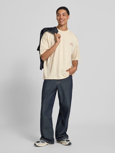 Männermodel trägt Oversized T-Shirt mit rückseitigem Print von REVIEW, cremefarben, Bio-Baumwoll-Mix, Logo-Print, Ganzkörperansicht von vorne.