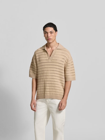 Männermodel trägt Relaxed Fit Poloshirt mit Viskose-Anteil von MAISON KITSUNÉ in Beige mit Lochmuster, Umlegekragen, Halbarm, Ganzkörperansicht von vorne.