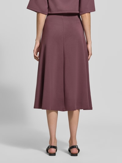Vrouwenmodel draagt Midirok met elastisch bund van Christian Berg Woman in bordeaux, gemaakt van elastische materiaalmix met modal, los model, midilengte, bandwijdte maat S 80 cm, geheellichaamsopname achteraan.