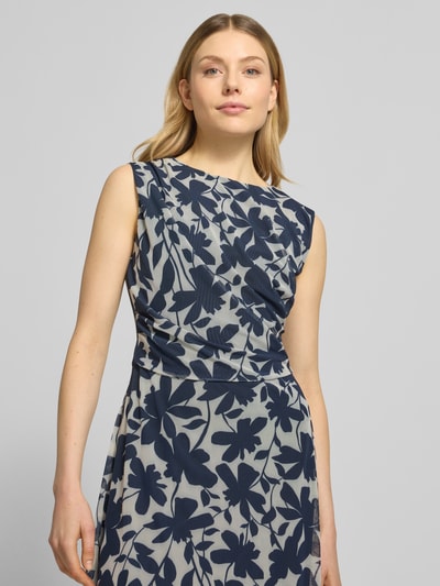Modelka kobieca nosi Regular Fit Midikleid mit floralem Allover-Print od Swing ze wzorem kwiatowym, krój regular fit, tkanina elastyczna, dekolt okrągły, bez rękawów, z marszczeniami, podszewka kryjąca, materiał o gładkiej teksturze, kolor granatowy na jasnym tle, zbliżenie na górną część ciała, widok z przodu.