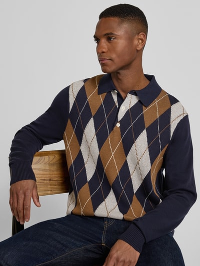 Męski model nosi Regular Fit Strickpullover aus reiner Baumwolle von Tommy Hilfiger w kratkę, dzianina, granat, brąz, biel, bawełna, długi rękaw, kołnierzyk polo, widok z przodu na górną część ciała.
