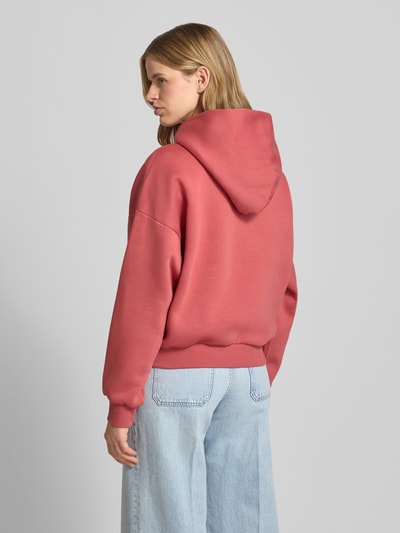 Frauenmodel trägt Hoodie mit Logo und Känguru-Tasche von REVIEW in Rosa, Baumwoll-Mix, Relaxed-Fit, glatte Struktur, Ganzkörperansicht Rückansicht.