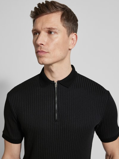 Męski model nosi Regular Fit Poloshirt mit Bio-Baumwoll-Anteil Modell 'FAVE' od SELECTED HOMME, czarny, krótki rękaw, materiał prążkowany, optyka jednolita, kołnierz polo, krótki zamek, ściągacze, nahaufnahme górnej części ciała.