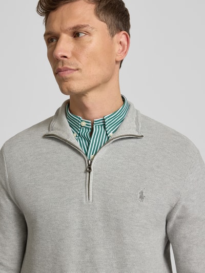 Męski model nosi Sweter z dzianiny z wyhaftowanym logo od Polo Ralph Lauren z bawełny, krój regular fit, prążkowane wykończenia, stójka, krótki zamek błyskawiczny, długość tyłu 70 cm, długość rękawa 68 cm, kolor jasnoszary, tekstura gładka; zbliżenie na górną część ciała.