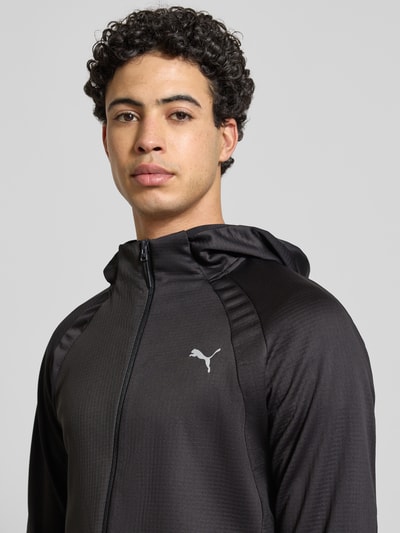 Männermodel trägt Regular Fit Trainingsjacke mit Logo-Print von PUMA PERFORMANCE in Schwarz mit Kapuze, Reißverschluss und Eingrifftaschen, Nahaufnahme Oberkörper.