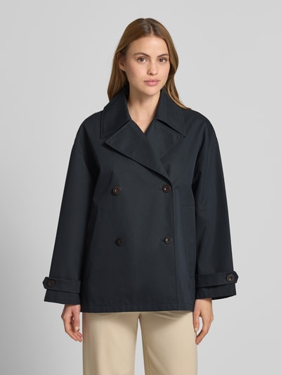 Modelka kobieca ma na sobie Trenchjacke mit Reverskragen Modell 'HEATHER' od G-LAB, prosty krój, ciemny kolor, widoczny guzikowy zapięcie, pasek na rękawie, długość tyłu w rozmiarze S: 70 cm, szerokość ramion w rozmiarze S: 48 cm, szerokość w klatce piersiowej w rozmiarze S: 52 cm, długość rękawa w rozmiarze S: 51 cm, całkowity widok z przodu