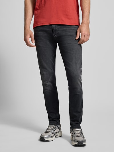 Männermodel trägt Slim Fit Jeans aus Baumwoll-Mix Modell 'AUSTIN' von Tommy Jeans in dunkler Denim-Optik, 5-Pocket-Design, Label Patch, Logo-Stitching, Nieten, Ganzkörperansicht von vorne.