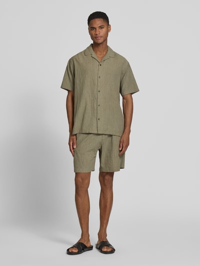 Männermodel trägt Regular Fit Freizeithemd mit Reverskragen von Jack & Jones Premium in Olivgrün, Struktur-Optik, Baumwoll-Elasthan-Mix, Knopfleiste, Ganzkörperansicht von vorne.