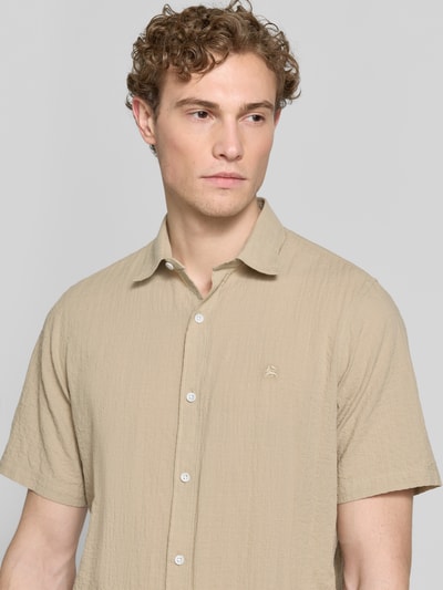 Męski model nosi Relaxed Fit Freizeithemd mit Logo-Stitching und Kentkragen od Lerros, seersucker, listwa guzikowa, wyhaftowane logo, zaokrąglony dół, długość tyłu w rozmiarze M: 75 cm, szerokość w rozmiarze M: 45 cm, długość rękawów w rozmiarze M: 25 cm, jasny beż, faktura seersucker, krótki rękaw, widok z przodu, zbliżenie na górną część ciała