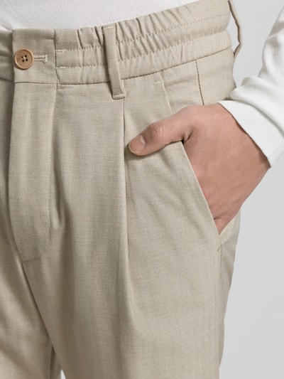 Mannenmodel draagt Stoffhose mit elastischem Bund van Drykorn, lichte beige tint, rechte fit, elastische tailleband, materiaal-mix met viscose, steekzakken, knoop- en ritssluiting, close-up opname van de heup en taille.