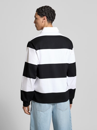 Männermodel trägt Relaxed Fit Poloshirt aus Baumwolle von CHAMPION mit schwarz-weißem Streifendesign, Label-Stitching, langärmlig, Ganzkörperansicht Rückansicht.