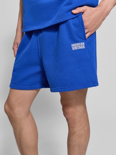 Männermodel trägt blaue Shorts mit Logo Modell 'PLIZZY' von American Vintage aus reiner Baumwolle im Relaxed-Fit, Nahaufnahme Oberschenkel.