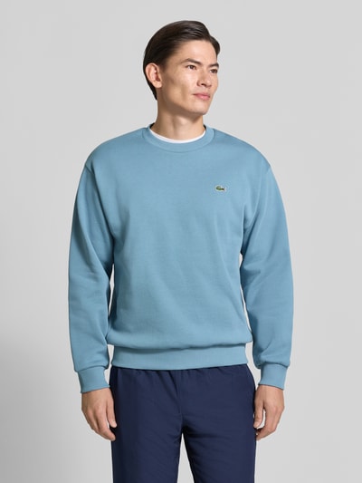 Männermodel trägt Regular Fit Sweatshirt aus Baumwoll-Mix von Lacoste in hellem Blau mit glatter Textur, Ganzkörperansicht von vorne.