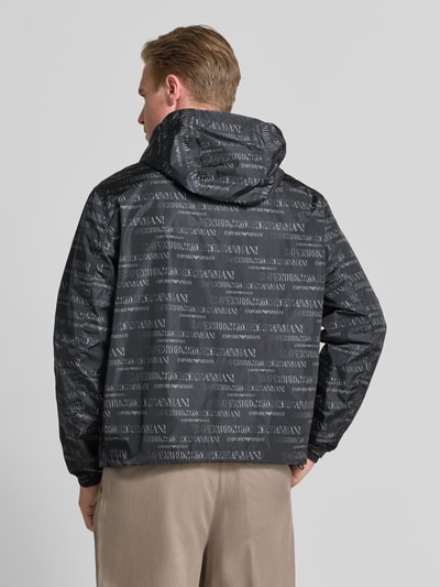 Männermodel trägt Jacke mit Logo-Muster und Zweiwege-Reißverschluss von Emporio Armani in Schwarz mit Kapuze, Regular-Fit, Rückenlänge 70 cm, Schulterbreite 58 cm, Brustweite 62 cm, Ärmellänge 66 cm, Ganzkörperansicht Rückansicht.