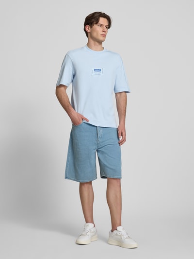 Männermodel trägt Regular Fit T-Shirt aus reiner Baumwolle Modell 'NURAZTI' von Hugo Blue in Hellblau, unifarben, Label Patch, Ganzkörperansicht von vorne.