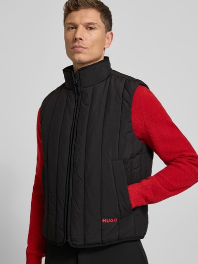 Männermodel draagt Regular Fit Steppweste uit waterafstotend materiaal model 'BRENO2611' van HUGO, zwart, met opstaande kraag en zijzakken, labelprint, unikleurig, Ganzkörperansicht von vorne.