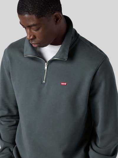 Männermodel trägt Regular Fit Pullover aus reiner Baumwolle von Levi's® in Dunkelgrün mit silbernem Reißverschluss, Nahaufnahme Oberkörper.