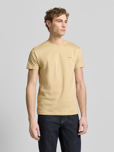 Männermodel trägt T-Shirt mit Label-Detail von Gant in Beige, aus reiner Baumwolle, gerader Schnitt, Rundhalsausschnitt, Ganzkörperansicht von vorne.