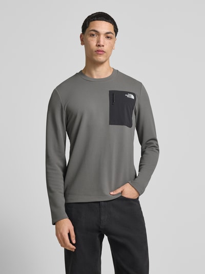 Männermodel trägt Langarmshirt mit Napoleontasche Modell 'KECHA' von The North Face, Elastischer-Material-Mix, Gerader-Schnitt, Rundhalsausschnitt, Label-Detail, Rückenlänge 67 cm bei Größe M, graue und schwarze Farbakzente, Ganzkörperansicht von vorne.