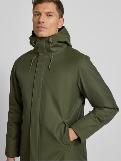 Männermodel trägt Regular Fit Parka aus Baumwoll-Mix von Barbour in Unifarben Oliv mit Kapuze, verdecktem Reißverschluss und seitlichen Eingrifftaschen, wasserabweisend, Label-Stitching, Nahaufnahme Oberkörper.