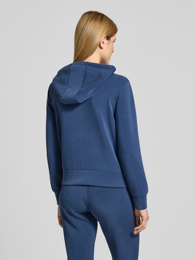 Vrouwenmodel draagt Regular Fit Sweatshirt met Logo-Applikation Modell 'Olympe' van Guess Activewear in blauw, elastische mix met modal, capuchon met tunnelkoord, rits, elastische boorden. Volledig zicht van achteren.