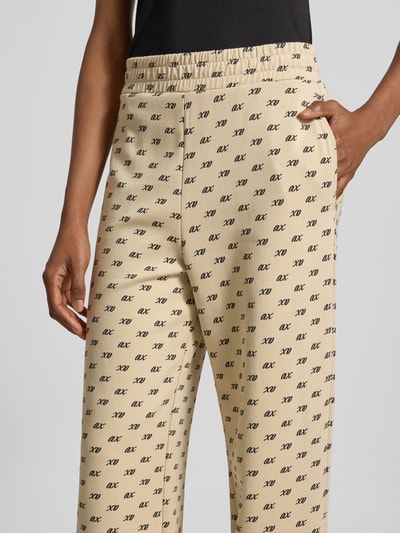 Frauenmodel trägt Wide Leg Sweatpants aus Baumwoll-Mix von Armani Exchange, hellbeige mit Allover-Logo-Print, Nahaufnahme Hüfte.