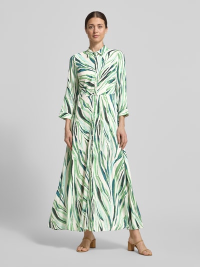 Frauenmodel trägt Hemdblusenkleid aus Reine Viskose Modell 'SAVANNA' von YAS mit grün-weißem Muster, Taillierter Passform, Midikleid, Kentkragen, Knopfleiste, 3/4-Arm, Rückenlänge 135 cm, Brustweite 42 cm, Ärmellänge 49 cm, Ganzkörperansicht von vorne.