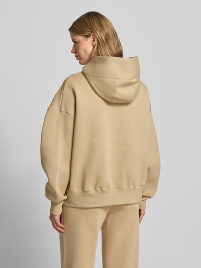 Frauenmodel trägt Oversized Hoodie mit Logo von Nike aus Baumwoll-Mix in Beige mit Känguru-Tasche, Ganzkörperansicht Rückansicht.