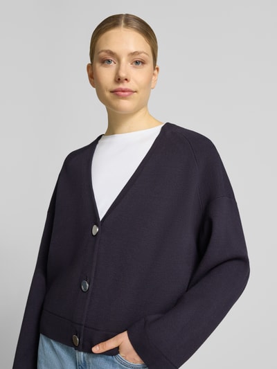 Frauenmodel trägt Strickjacke aus Viskose-Mix mit V-Ausschnitt von Comma in Dunkelblau, Relaxed-Fit, Knopfleiste, Ganzkörperansicht von vorne, Rückenlänge 54 cm, Ärmellänge 47 cm, Größe 36.