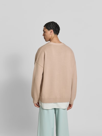 Männermodel trägt Oversized Cardigan aus Schurwoll-Mix von MM6 Maison Margiela in Beige mit Strick-Optik, Ganzkörperansicht Rückansicht. Rückenlänge 78 cm, Schulterbreite 48 cm, Ärmellänge 69 cm, Oversized-Fit, V-Ausschnitt und durchgängige Knopfleiste.