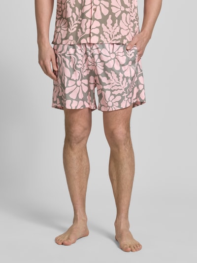 Männermodel trägt Badehose im Allover-Look Modell 'Melo' von BOARDIES, Regular Fit, rosa-graues Blumenmuster, Ganzkörperansicht von vorne.