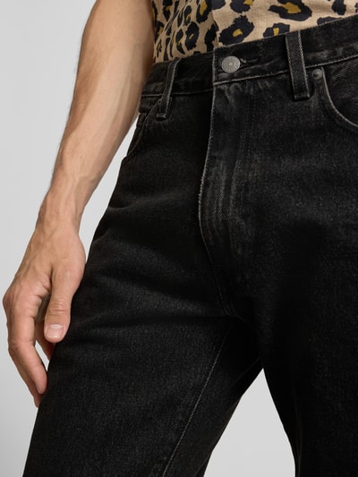 Mężczyzna nosi czarne, matowe jeansy z prostymi nogawkami Straight Leg Jeans aus reiner Baumwolle Modell '555®' von Levi's®, zbliżenie na biodra i rękę.