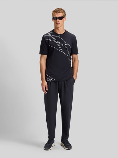 Mannelijk model draagt Tapered Bundfaltenhose met halvelastische tailleband Modell 'CONVERT-PLEAT' van BOSS Green, effen zwart, 4-way stretch, met persvouwen, tunnelkoord, riemlussen en steekzakken, geheellichaamsvooraanzicht.