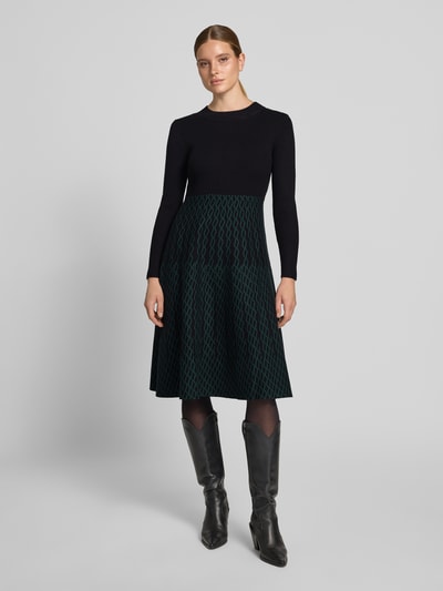 Vrouwenmodel draagt Knielanges Kleid mit Rundhalsausschnitt van Apricot, zwarte top, groene rok met patroon, viscosemix, getailleerd model, knielengte, ruglengte maat S 107 cm, borstwijdte maat S 35 cm, mouwlengte maat S 63 cm, geheel van voren te zien.