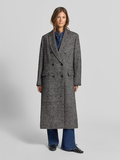 Frauenmodel trägt Relaxed Fit Mantel mit Woll-Anteil von MYON in Grau, doppelte Knopfleiste, Pattentaschen, Ganzkörperansicht von vorne.