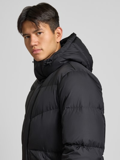 Männermodel trägt Regular Fit Steppmantel mit Kapuze von Marc O'Polo DENIM in Schwarz, glatte Oberfläche, Nahaufnahme Oberkörper.