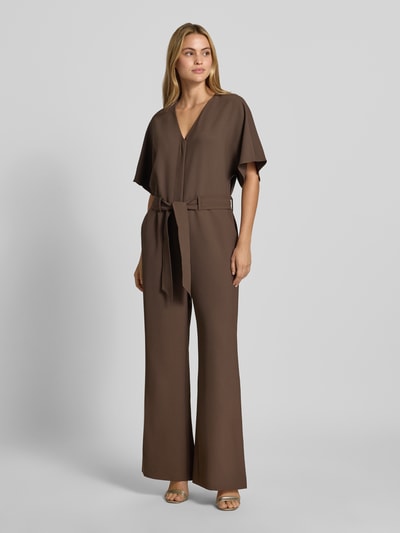 Kobiece modelka nosi kombinezon Jumpsuit mit V-Ausschnitt Modell 'Lehila' od MOS MOSH, brązowy, taliowany krój, całkowita długość 149 cm, Rękaw o dł. 1/2, Długość tyłu w rozmiarze S: 46 cm, Szerokość w rozmiarze S: 50 cm, Długość rękawów w rozmiarze S: 40 cm, Długość wewnętrzna nogawki w rozmiarze S: 76 cm, Ganzkörperansicht von vorne