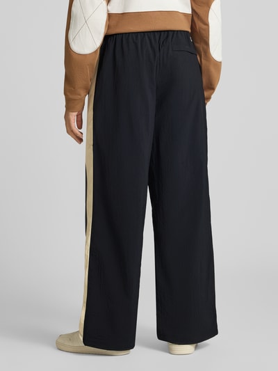 Männermodel trägt Relaxed Fit Sweathose mit Label-Detail von Nike in Schwarz mit beigem Seitenstreifen, Herren Sweathose, Ganzkörperansicht Rückansicht.