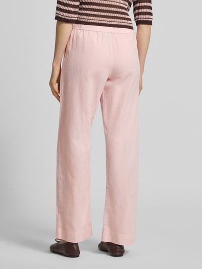 Frauenmodel trägt Stoffhose mit Leinen-Anteil und Eingrifftaschen von Neo Noir, ausgestellter Schnitt, Modell 'Sonar', Lockerer-Schnitt, pastellrosa, feine Textur, Ganzkörperansicht Rückansicht. Damen Stoffhose aus Baumwoll-Mix mit Leinen-Baumwoll-Anteil, elastischer Bund, französische Eingrifftaschen, Bundweite 36 cm, Innenbeinlänge 79 cm, Modell Neo Noir.