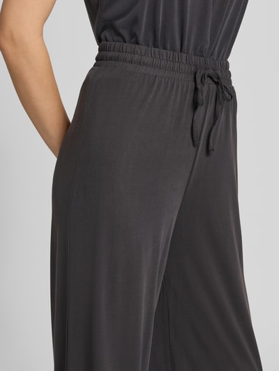 Frauenmodel trägt Weite Hose aus Viskose-Mix Modell 'ANORA' von PIECES in Dunkelgrau mit glatter Textur, Nahaufnahme Hüftbereich. Damen Weite Hose von PIECES.